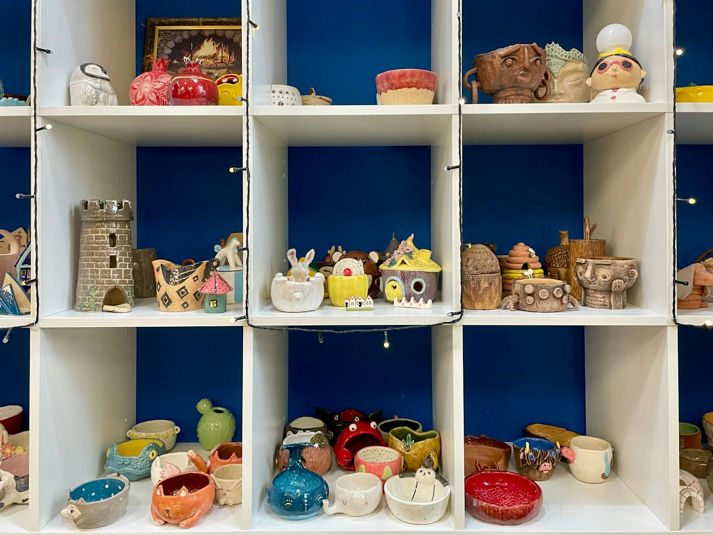 Vasi e oggetti decorativi in ceramica fatti a mano esposti su mensole bianche.