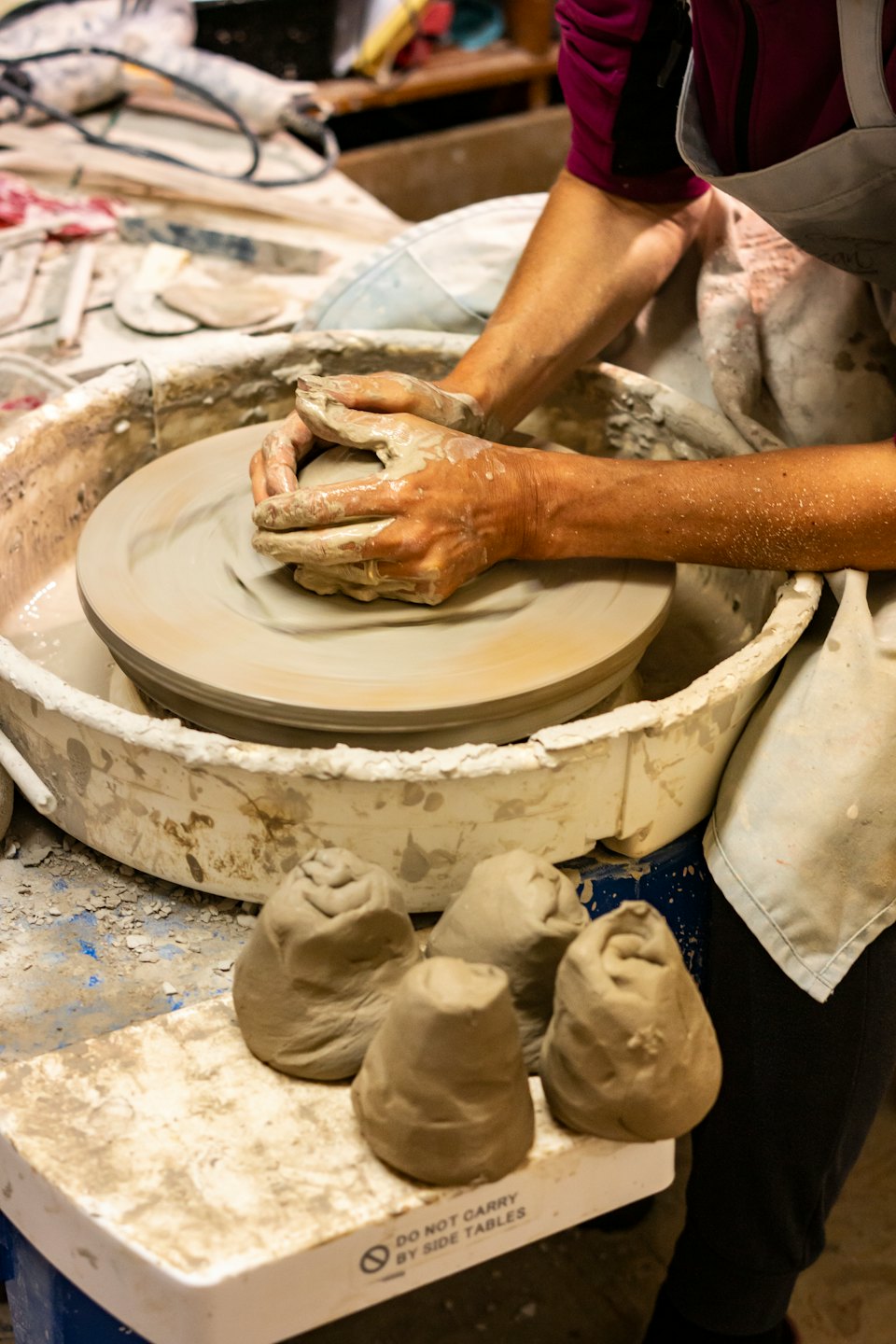 Mani sporche di argilla bagnata che modellano un vaso su un tornio da vasaio.