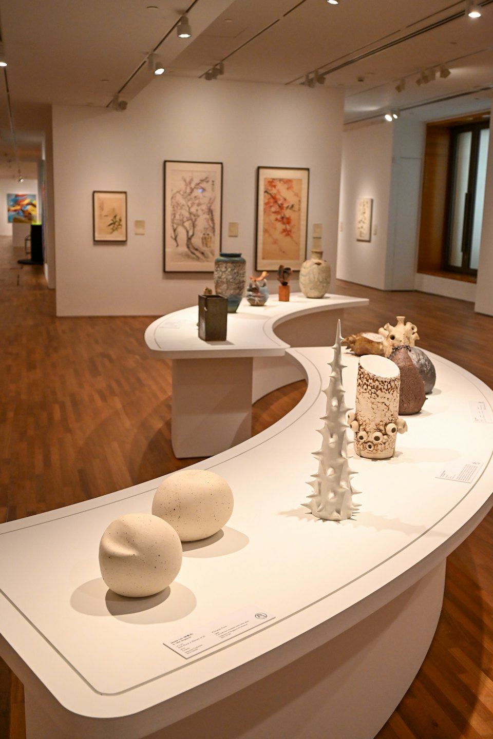 Sculture in ceramica e dipinti esposti in una galleria d'arte moderna.